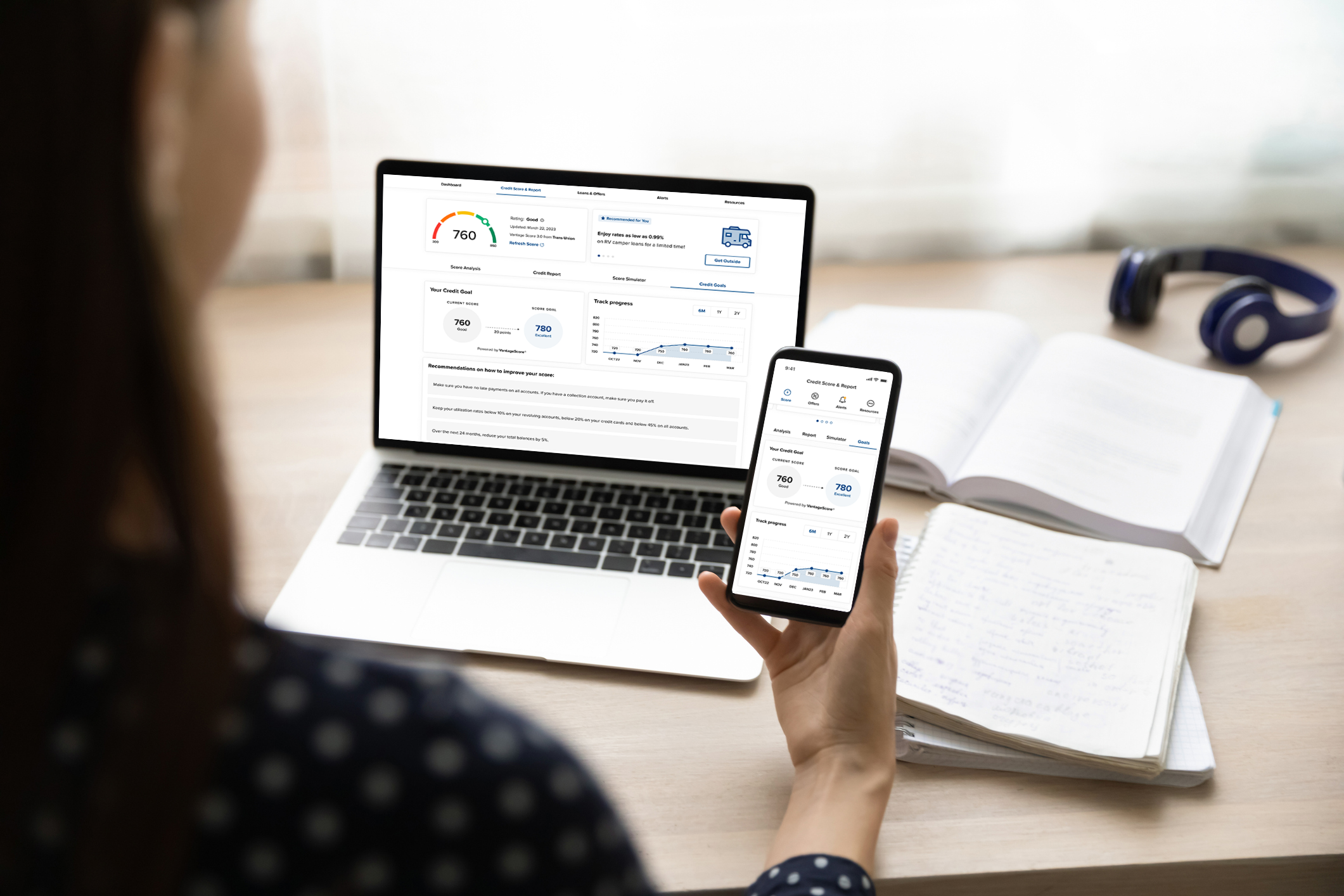 Woman checking her credit score on mobile device and laptop while sitting at a desk in her home
