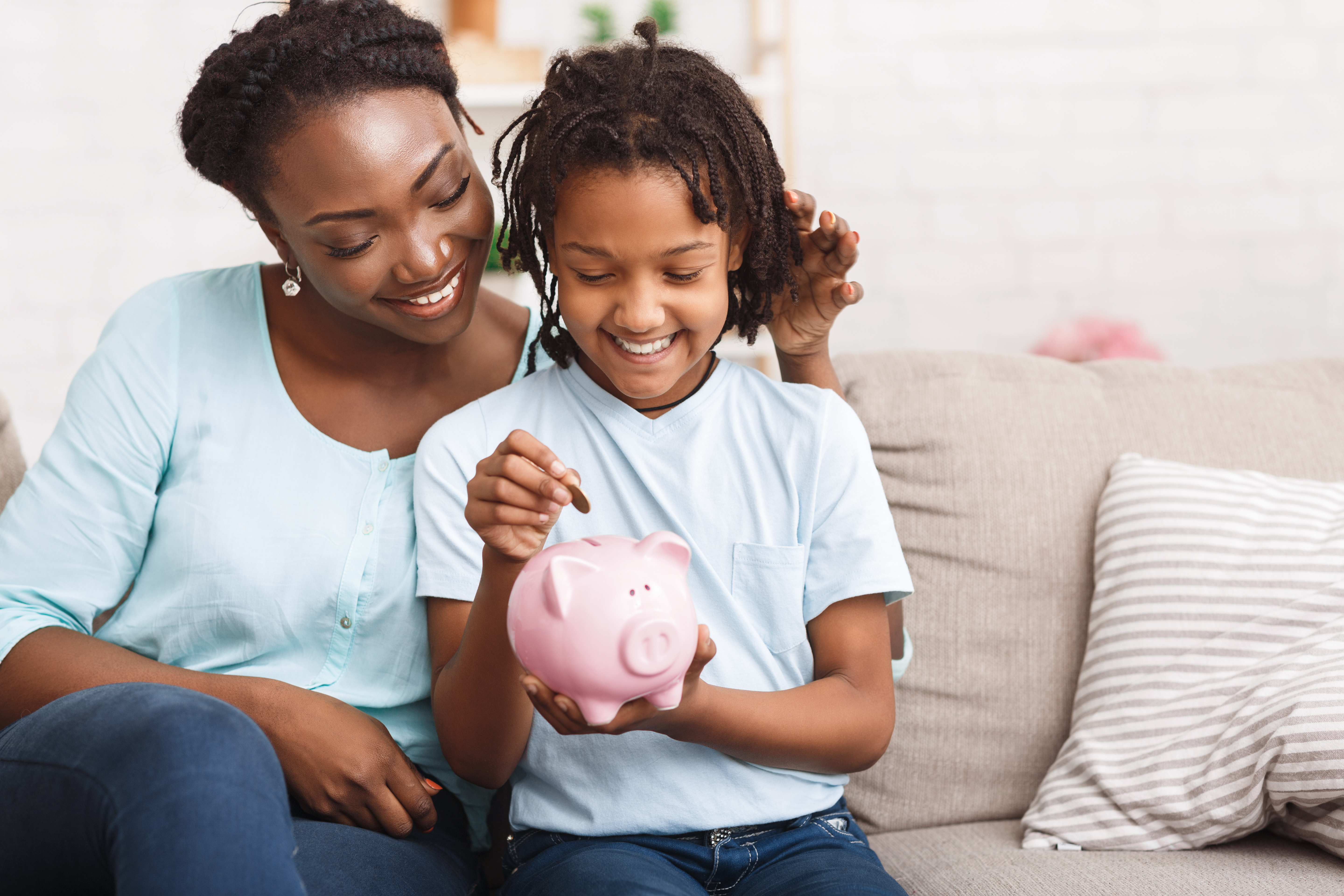 Mom and daughter at home on the couch with a piggy bank to save money