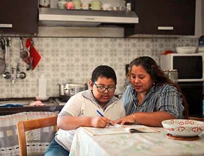 Mother helps her son with his homework at the kitchen table.