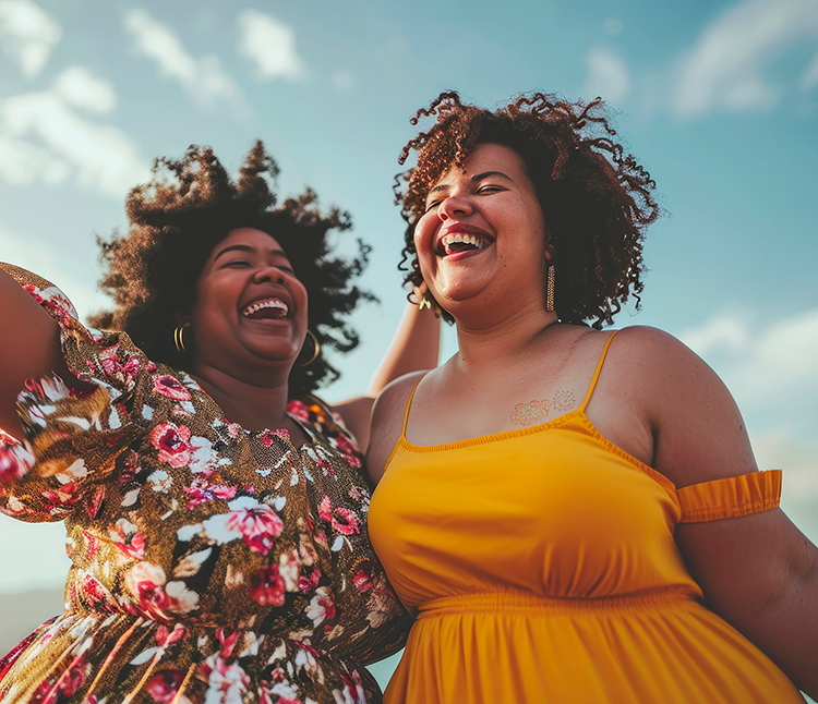 Two women wearing dresses happily jumping outside.